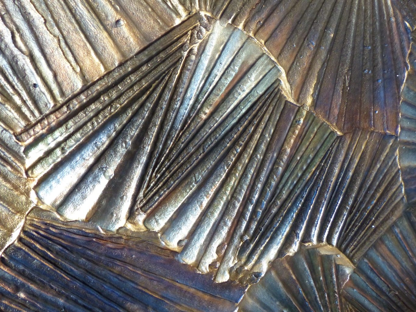 Détail du travail de matière et du relief d’un mur artistique sculpté révélant des nuances métalliques et des effets de lumière.